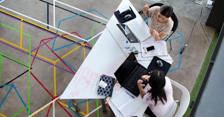 Two coworkers using their devices at a shared desk.