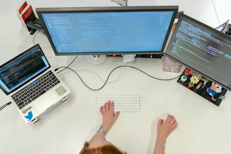 A person working at their desktop with a laptop and two monitors.