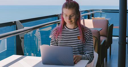 A woman working remotely outside near the ocean while using her laptop.