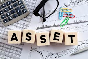 Blocks spelling 'ASSET' on top of financial charts, calculator, glasses, and paperclips.