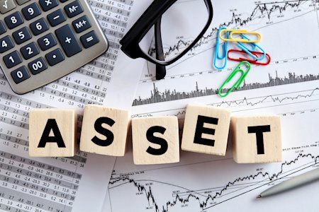 Blocks spelling 'ASSET' on top of financial charts, calculator, glasses, and paperclips.