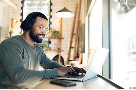 A man using a laptop and wearing headphones in a modern café, representing a seamless remote onboarding experience.