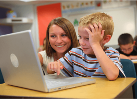 Teacher sitting beside a student both looking at a laptop screen