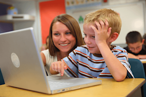 Teacher sitting beside a student both looking at a laptop screen