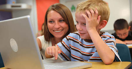 Teacher sitting beside a student both looking at a laptop screen