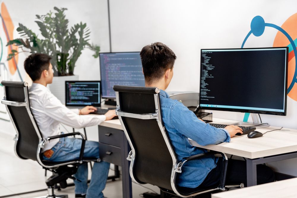 Two coworkers typing code on their computers.