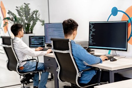 Two coworkers typing code on their computers.