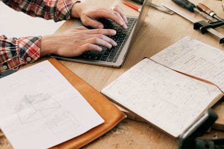 A person in a manfucturing facility types on a laptop.