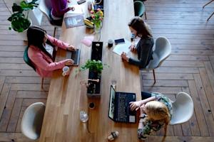 A group of workers on their laptops at a shared conference table.