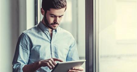 Man standing near window using a tablet with his finger