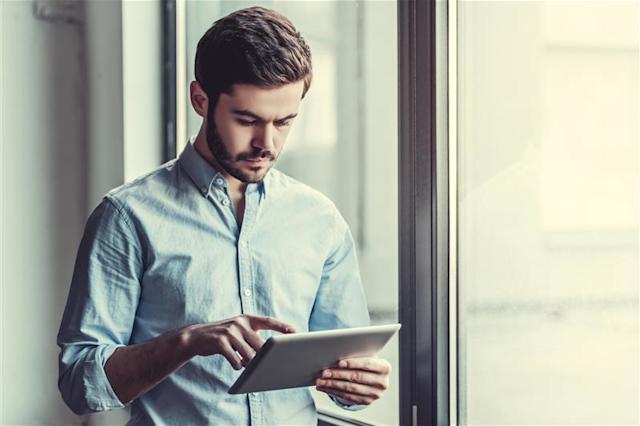 Man standing near window using a tablet with his finger