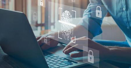 Hands typing on a laptop with a fingerprint scan and security icons.