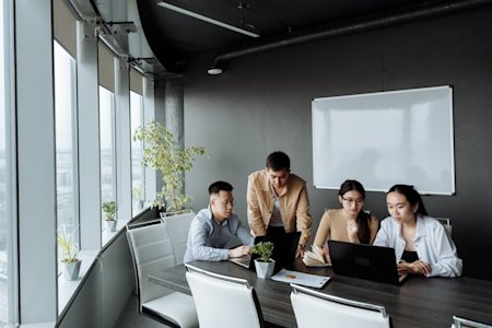Coworkers in a meeting at a conference table with their computers.
