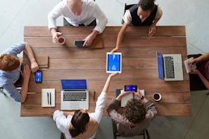 Co-workers sitting around a conference table using various devices.