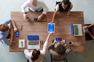 Co-workers sitting around a conference table using various devices.