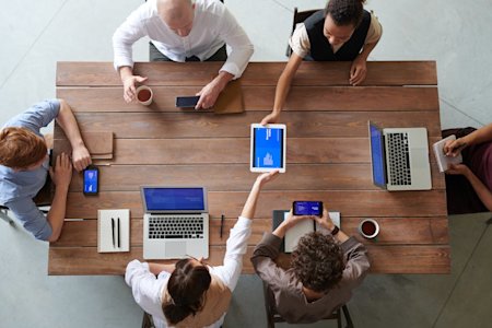 Co-workers sitting around a conference table using various devices.