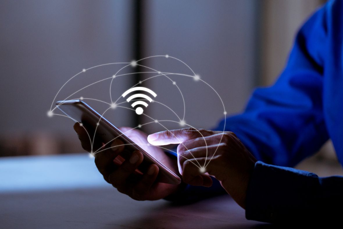 A person in a blue shirt uses a smartphone, with a glowing Wi-Fi symbol and network lines digitally superimposed above the device, representing wireless connectivity.