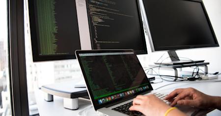 A computer with two additional monitors showing lines of code.
