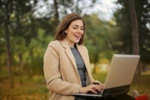 A smiling woman in a park working remotely on her laptop by using Splashtop to remotely access her work computer.