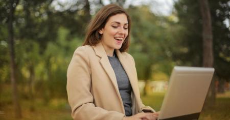 A smiling woman in a park working remotely on her laptop by using Splashtop to remotely access her work computer.
