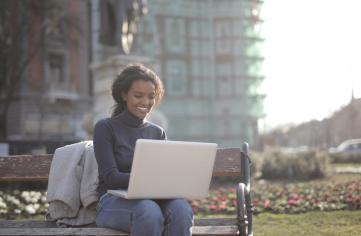 A smiling woman sitting on a park bench using a laptop.