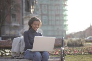 A smiling woman sitting on a park bench using a laptop.