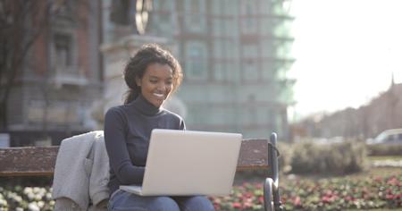 A smiling woman sitting on a park bench using a laptop.