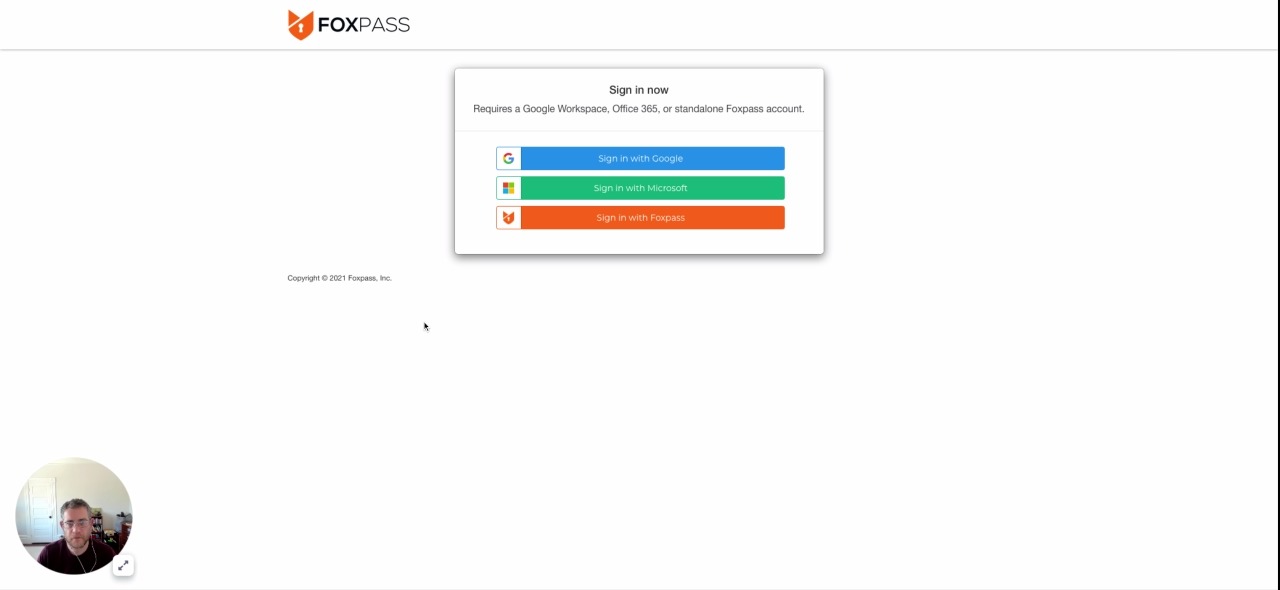 Screenshot of a Foxpass login page with options to sign in using Google, Microsoft, or Foxpass. A small video call window shows a person in the bottom left corner.