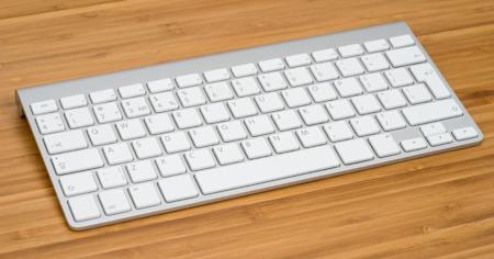 A bamboo desk with a white Apple keyboard resting on it