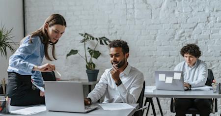 Two coworkers looking at a computer screen and talking to each other.