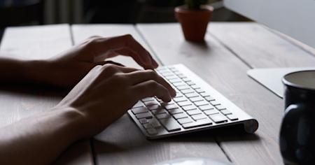 A person typing on a desktop computer keyboard.