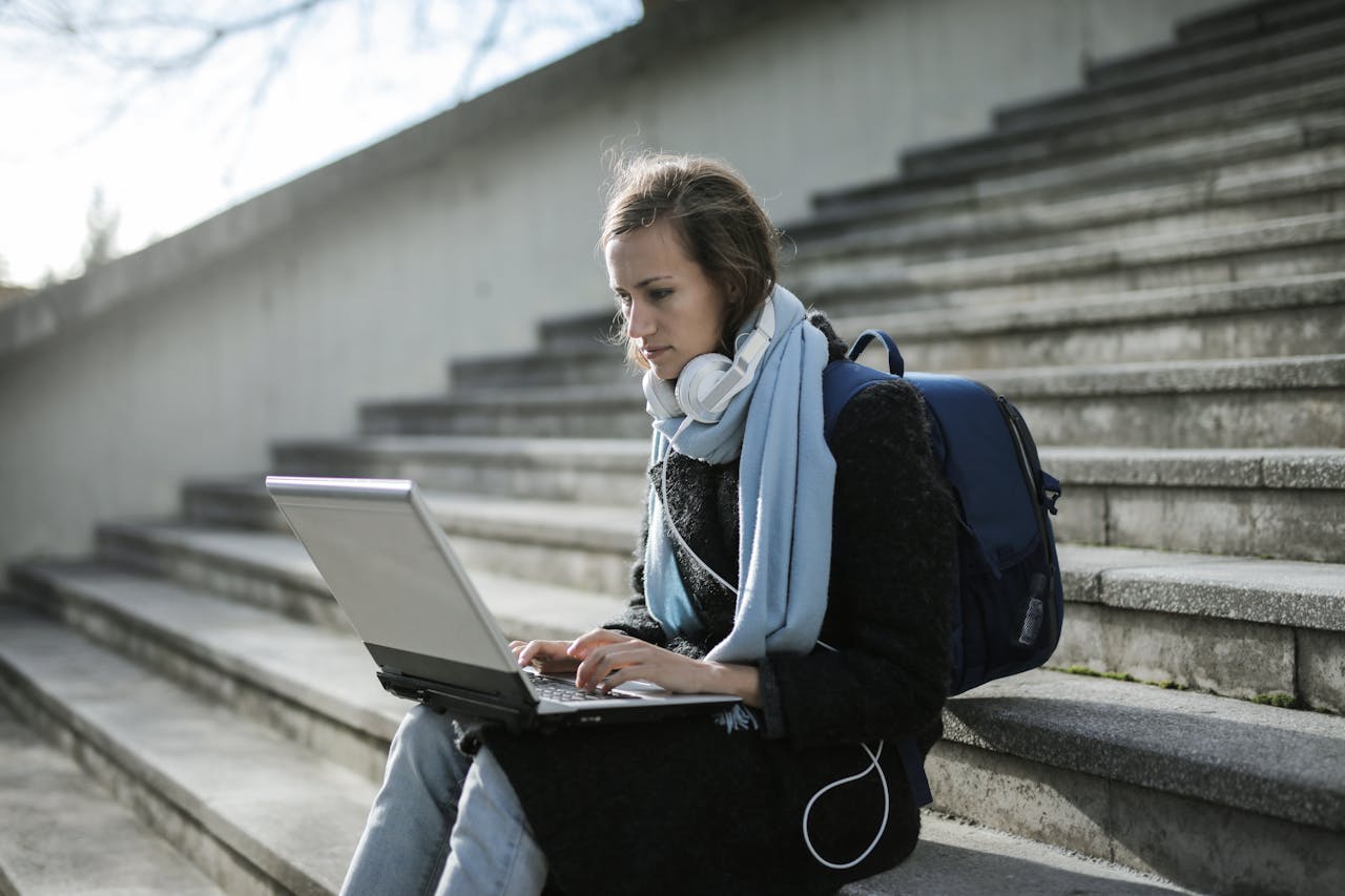 A woman outside sitting on steps and using her laptop.