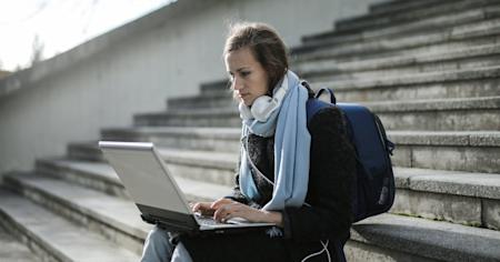 A woman outside sitting on steps and using her laptop.