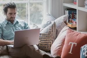 A man sitting on a couch at home working remotely from a laptop by using Splashtop.