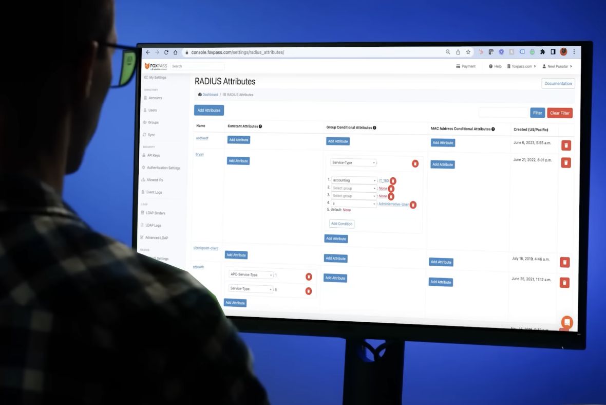 A person in glasses looks at a computer monitor displaying a web interface for managing RADIUS attributes, with various settings and options visible on a blue background.