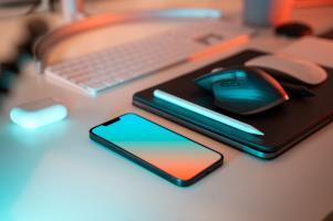 A smartphone, laptop, mouse, and keyboard sitting on a desk.