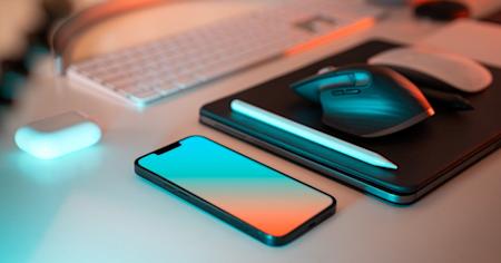 A smartphone, laptop, mouse, and keyboard sitting on a desk.