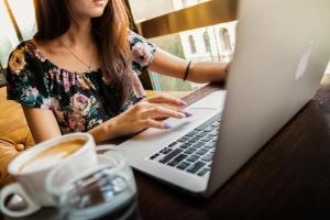 A woman sitting at a desk working on a laptop and with a cup of coffee.