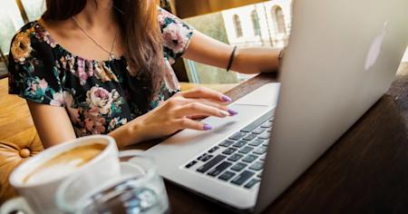 A woman sitting at a desk working on a laptop and with a cup of coffee.