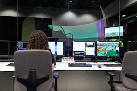 A person sitting at a desk with several computers and monitors.