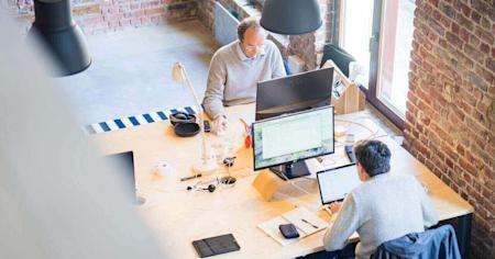 Two workers at their workstations using their computers in an office.