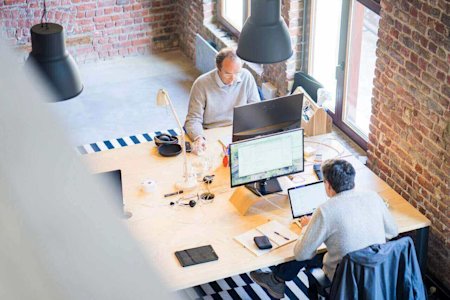 Two workers at their workstations using their computers in an office.
