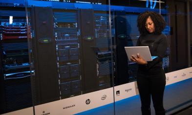 An IT Leader on her laptop standing in a server room.