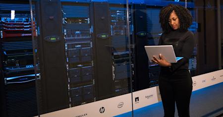 An IT Leader on her laptop standing in a server room.