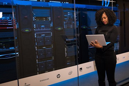 An IT Leader on her laptop standing in a server room.