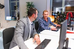 Two employees talking to each other and working on their computers.
