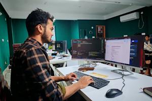 A man working on a computer with code on-screen in an office.