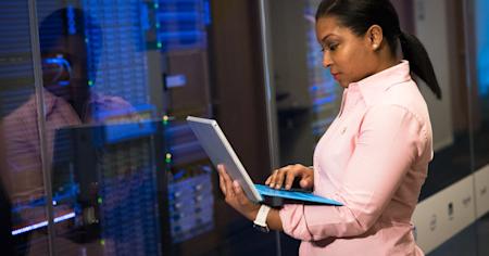 An IT worker using a laptop while standing near servers.