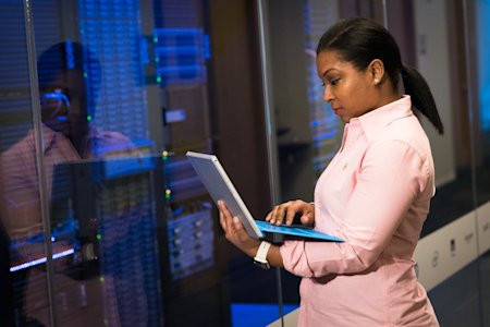 An IT worker using a laptop while standing near servers.
