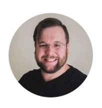 A man with short brown hair, glasses, and a beard, smiling at the camera. He is wearing a black shirt and is pictured against a plain light background in a circular frame.